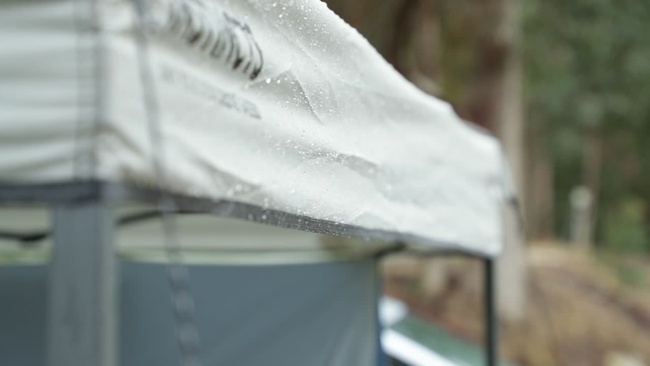 A slow motion handheld shot of light raining falling on a camp gazebo and the water falling down in