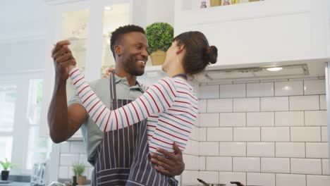 pareja feliz diversa con delantales azules y bailando en la cocina