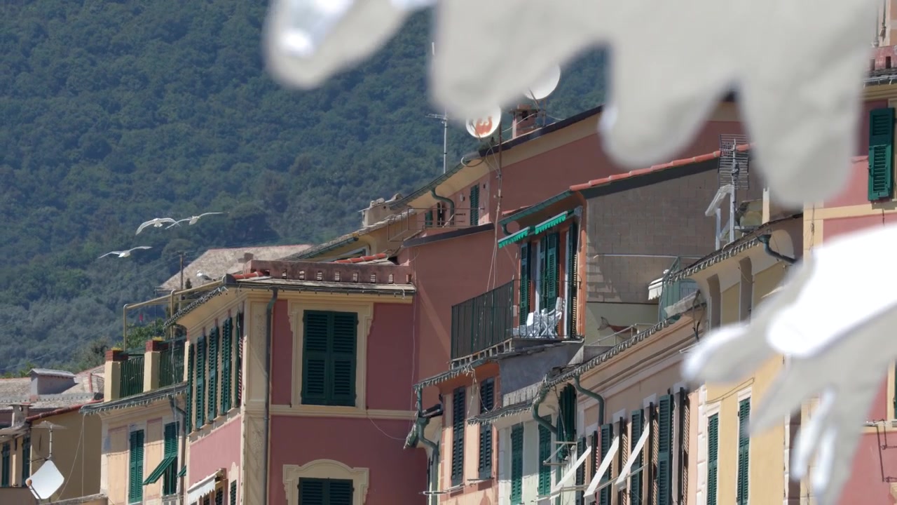 Vivaci facciate color terracotta e persiane verdi si ergono dietro biancheria bianca che sventola al vento.