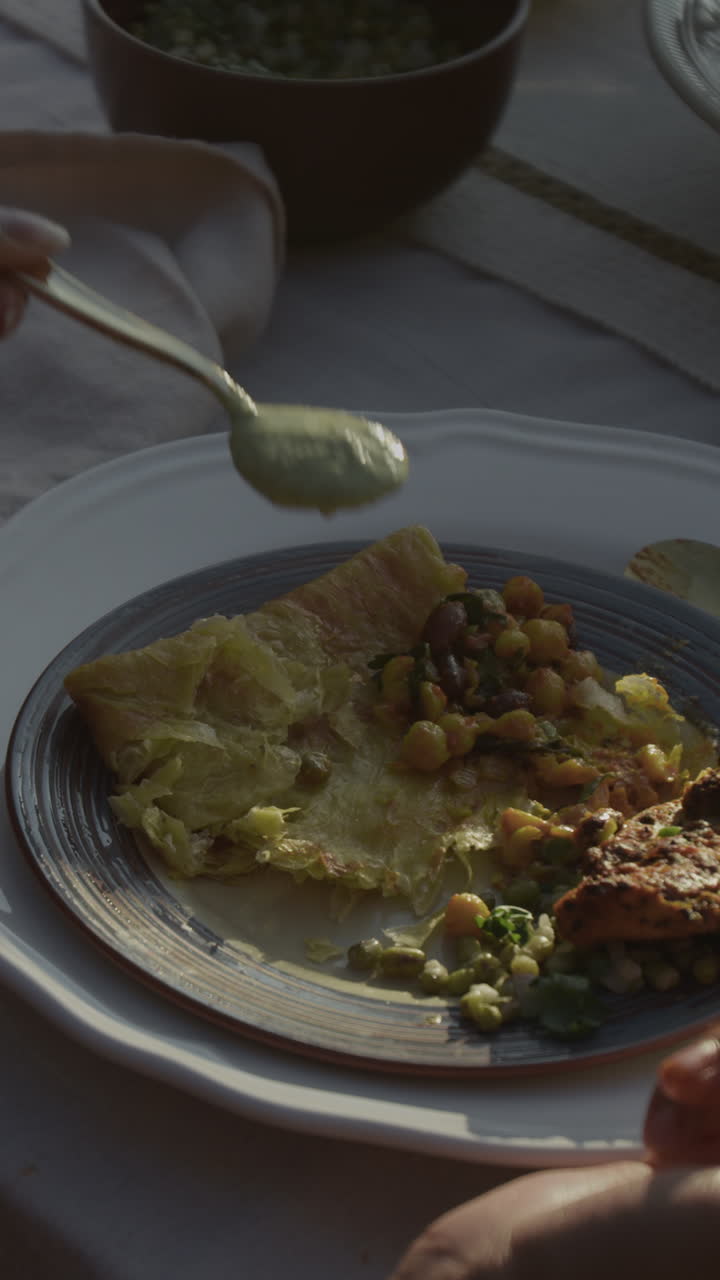 Close-up of a hand serving a healthy meal with chickpeas and green sauce on a plate