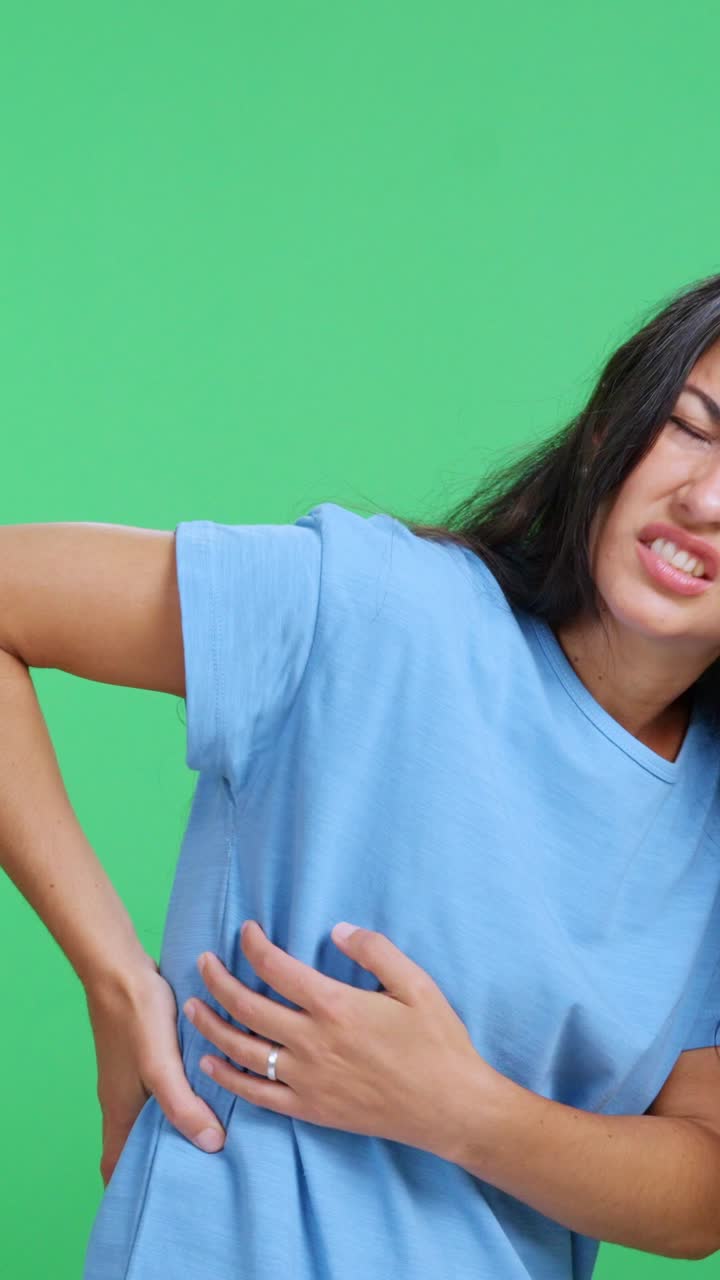 Woman suffering from severe back pain against a green screen