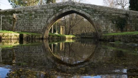 Serene-bridge-reflection-in-shallow-river-water-below-medieval-roman-bridge-in-Spanish-Countryside