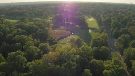 tracking-left-over-a-golf-course-road-and-trees-at-sunset