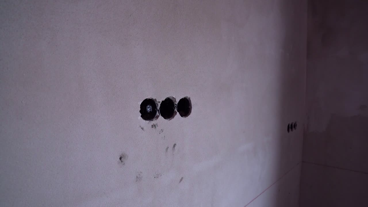 Electrical outlet holes drilled into bare plaster wall in unfinished residential interior