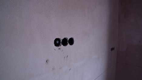 electrical outlet holes drilled into bare plaster wall in unfinished residential interior
