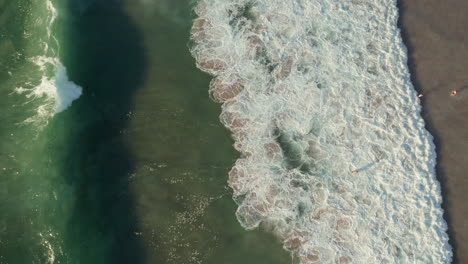 vertical shot of foamy ocean waves crashing with tourist at llandudno beach in cape town, south africa