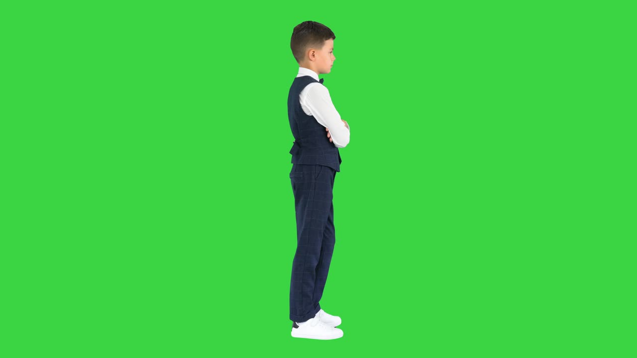 Confident young boy in bow tie and vest crossing his arms and putting hands in his pockets on a Green Screen, Chroma Key