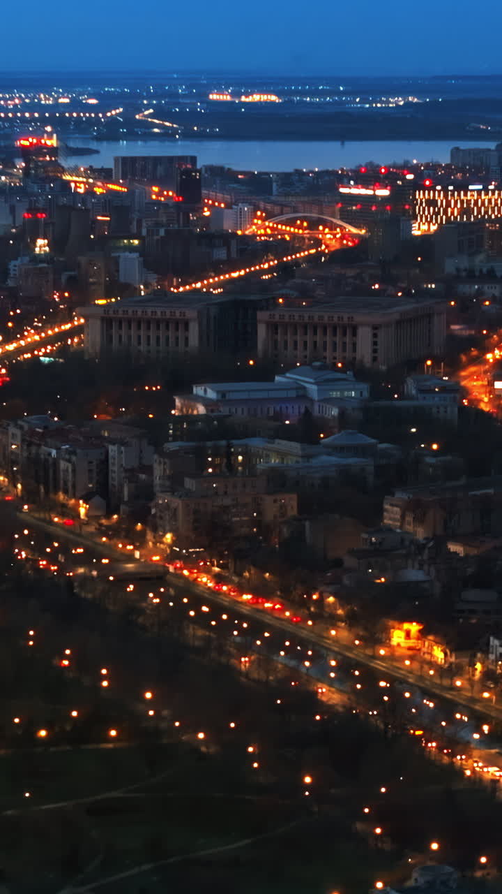 Vertical aerial drone view of illuminated Bucharest cityscape in the evening. Moving traffic. Blue hour, Romania