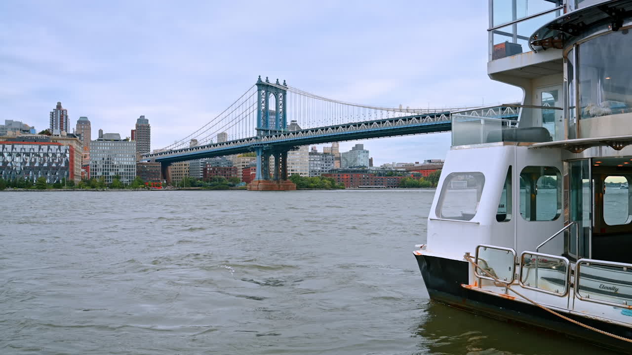 Large riverboat stands on the East River waterscape. The Manhattan Bridge at backdrop. Cloudy day in New York, USA