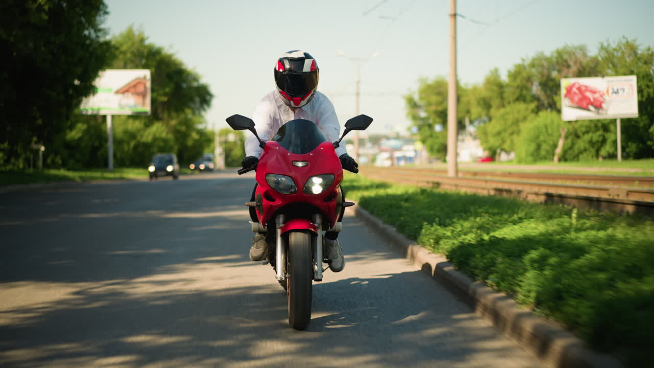 헬을 착용 한 오토바이 운전자 는 도로 근처 에 있는 빨간색 전력 자전거 를 타고 빨리 달린다. 자동차 는 불빛 을 켜고 흐릿 한 배경 에 보이며, 멀리 에서 표지판 도 보인다.