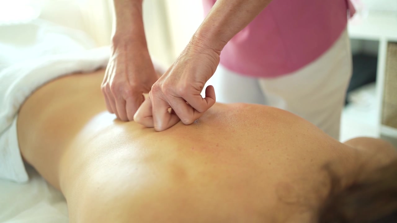 Osteopat masserer ryggen med hænder på klinik.