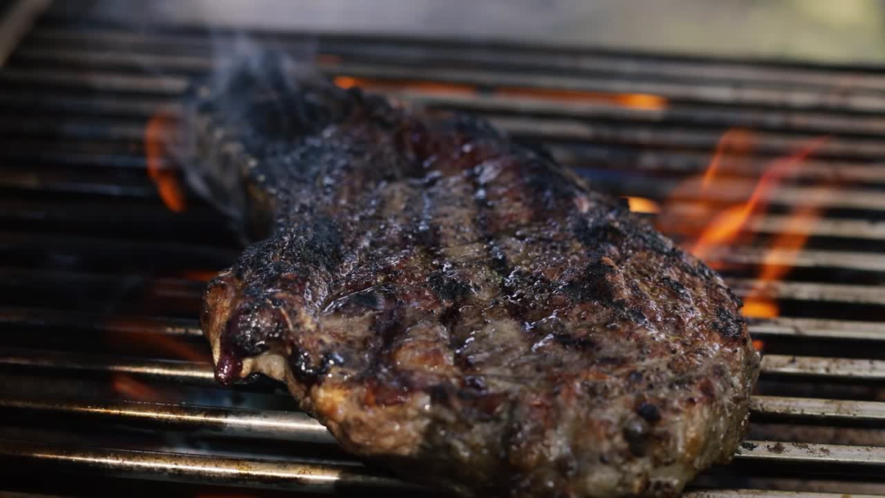 chef volviendo bistec cocido en una parrilla con llama alta, de cerca