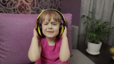 Little-child-girl-in-headphones-enjoying-listen-music.-Dancing-on-sofa-at-home