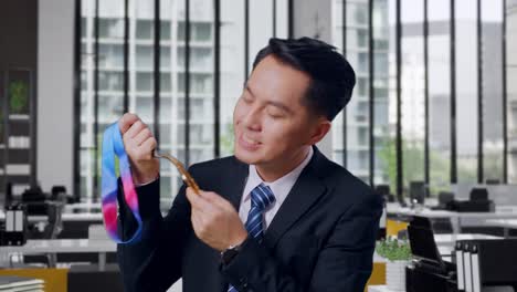 close up of asian business man in a suit and tie kissing a gold medal in his hand being proud winning as the first winner in office