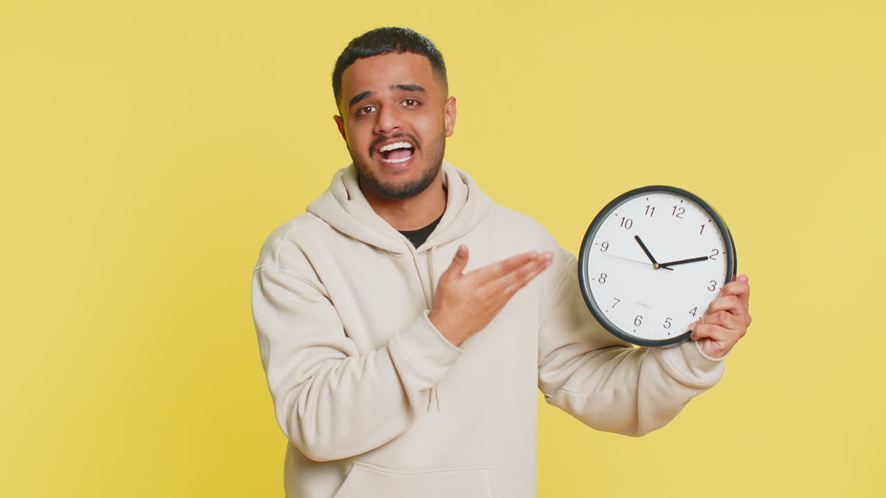 Indian young man with anxiety checking time on clock running late to work being in delay deadline