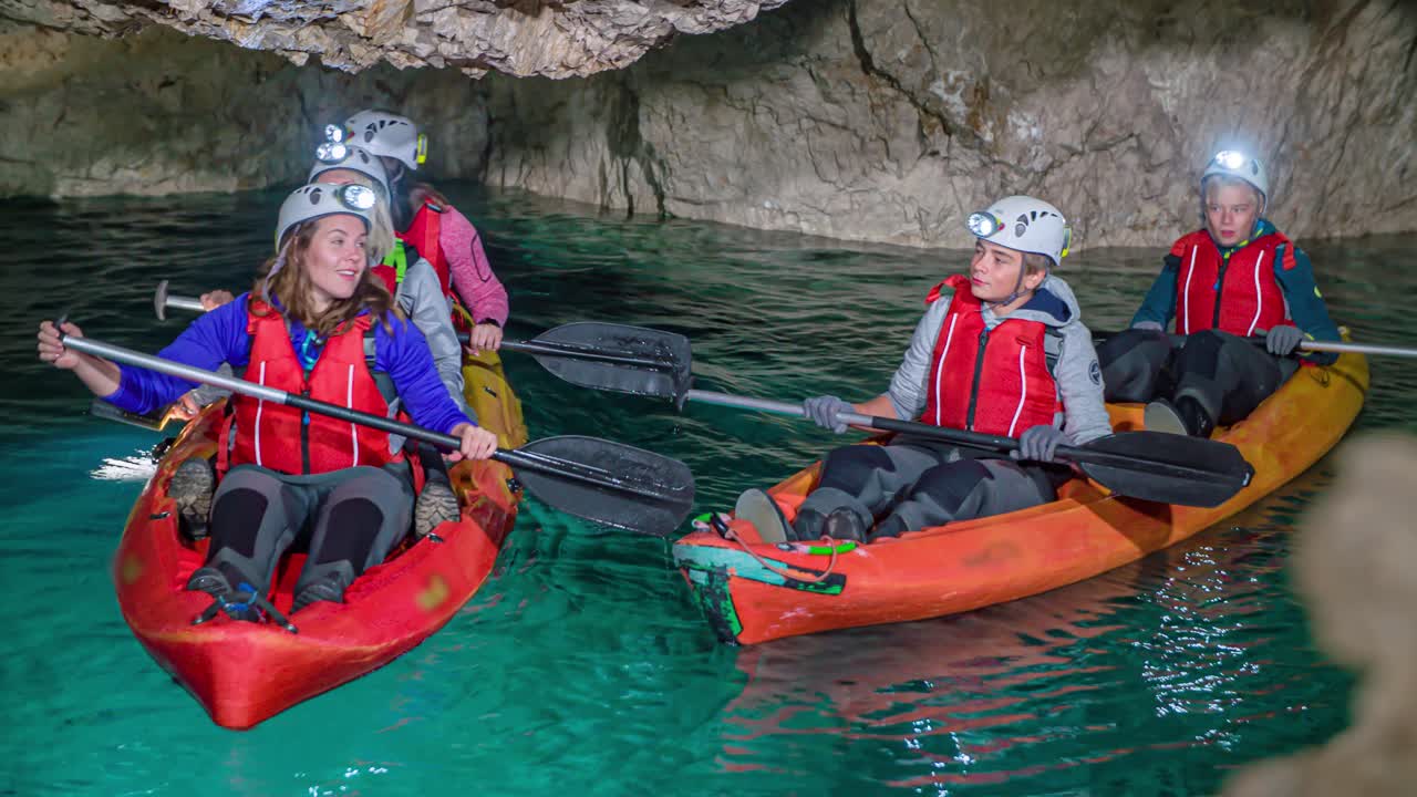 Caucasian tourists sitting on kayaks with paddles jump and listen to echo sound inside underground mining cave, close up pan