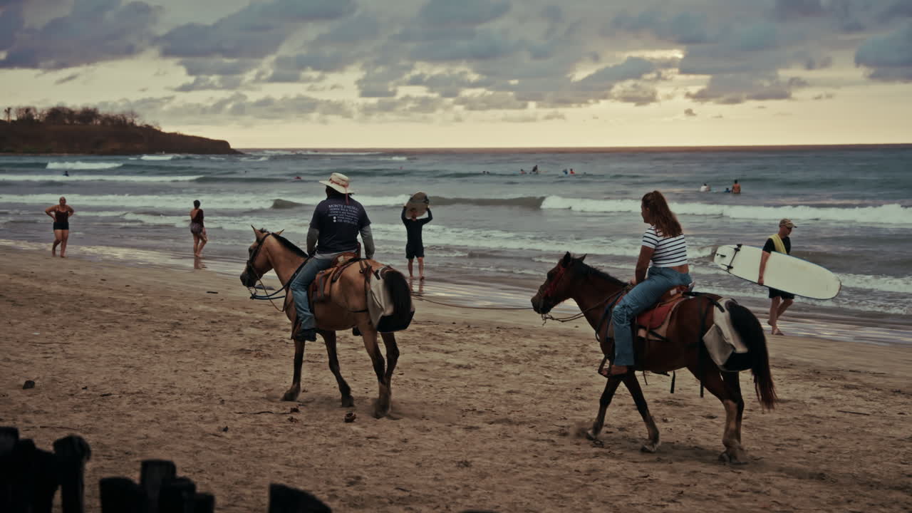Slow motion panoramic view of Tamarindo beach in Costa Rica. People have a good time and horseback riding on the beach. View of the tropical beach at sunset. Waves coming to the shore.