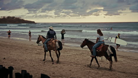 slow motion panoramic view of tamarindo beach in costa rica. people have a good time and horseback riding on the beach. view of the tropical beach at sunset. waves coming to the shore.