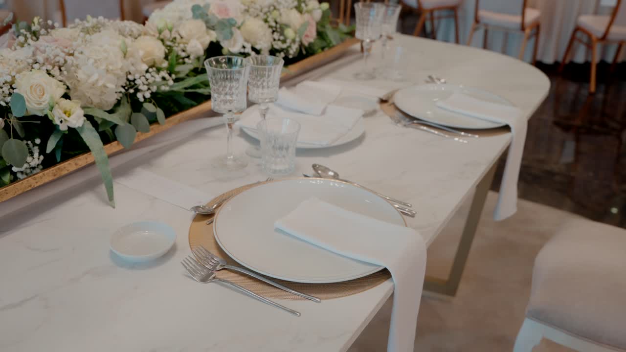 elegante mesa con pieza central floral, vasos de cristal y platos blancos en el interior