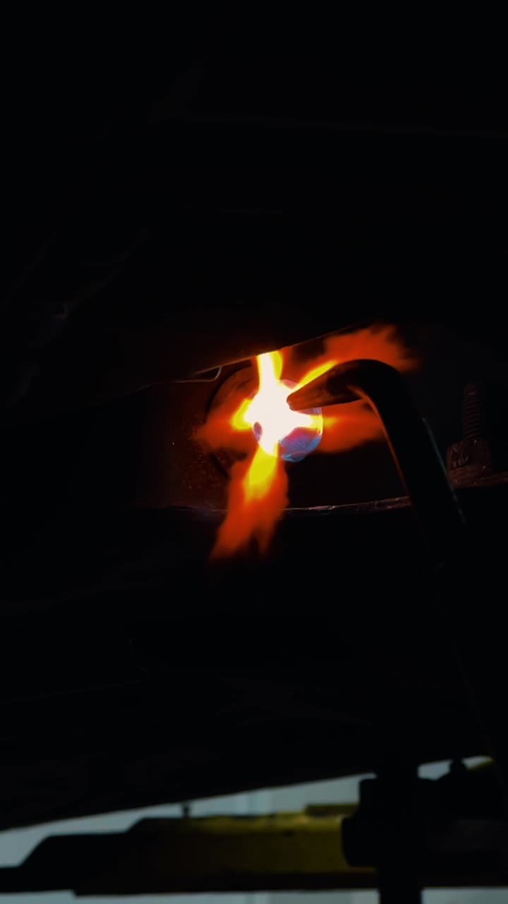Using welding torch to heat metal part in dark workshop. Close up of a gas welding torch flame heating a metal bolt and component under a vehicle chassis