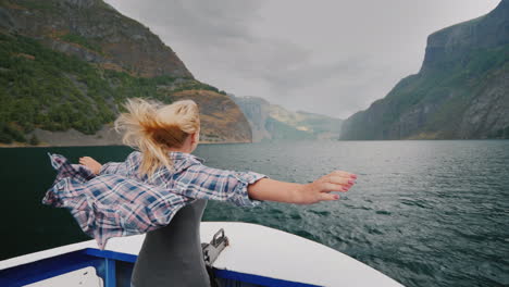 a free woman stands with her hands to the sides on the bow of a cruise ship traveling the fjords of