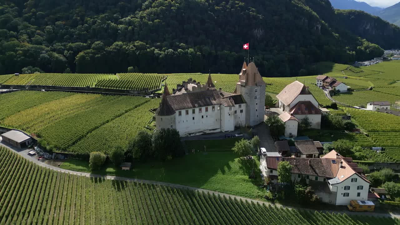 Reveal drone shot of beautiful Aigle Castle with Swiss flag waving in Vaud Switzerland