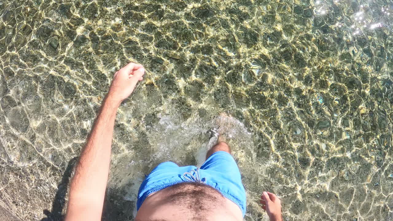 Caucasian man walking in the Aegean sea and starts swimming. Holding camera above the head, slow motion. Greece