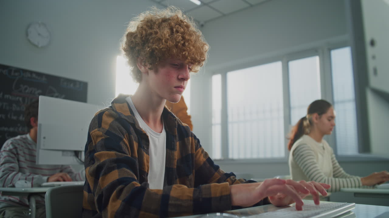Curly Haired Handsome Young Man in Sunny Computer Lab is Concentrating on Work at Computer