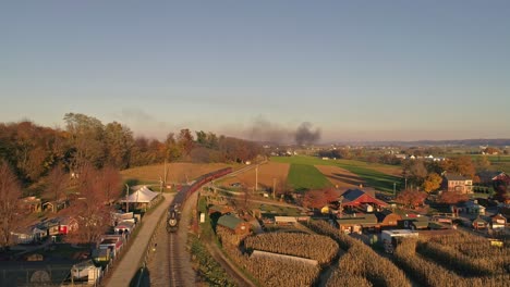 Vista-Aérea-De-Una-Antigua-Locomotora-De-Vapor-Que-Se-Acerca-Tirando-De-Los-Coches-De-Pasajeros-Y-Soplando-Humo-Y-Vapor-Durante-La-Hora-Dorada-A-última-Hora-De-La-Tarde