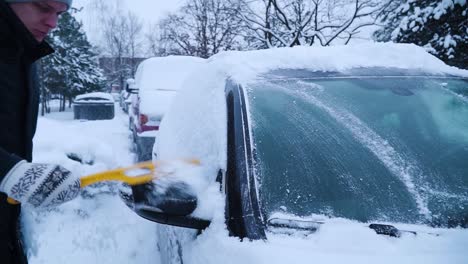 Der-Junge-Mann-Reinigt-Im-Winter-Die-Front--Und-Seitenfenster-Des-Autos-Mit-Einer-Gelben-Bürste-Vom-Schnee