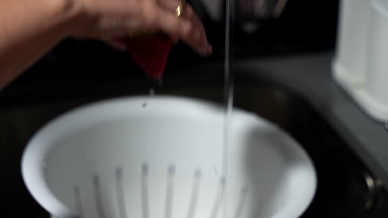 Focused hand under running tap water rinsing fresh strawberries in kitchen sink