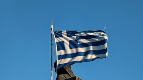 greek flag waving against clear blue sky with monument zagorian women pindos