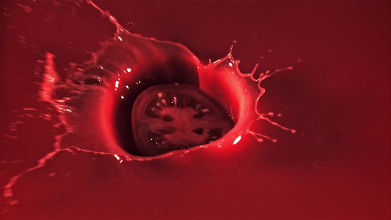 Tomatskive falder og sprøjter ned i rød væske i slowmotion