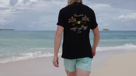 young blond haired caucasian man walking away from camera on tropical beach in asia in ultra slow motion