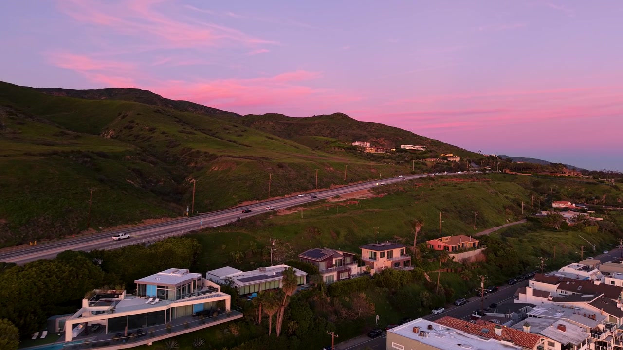 Il drone si inclina verso l'alto per rivelare il cielo al tramonto di Malibu sopra la costa del Pacifico, con sfumature dorate e rosa che si diffondono all'orizzonte in una rivelazione cinematografica della California.