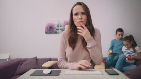 rostro de madre de negocios mirando el monitor con los niños jugando en el fondo