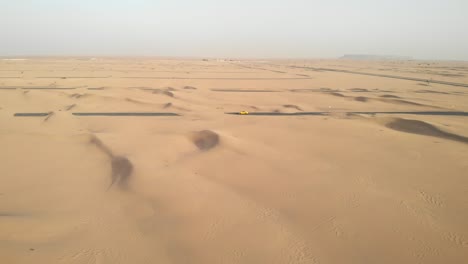 Aerial-circular-shot-with-a-drone-of-a-sports-car-in-the-middle-of-desert-roads-covered-with-sand-in-Dubai,-United-Arab-Emirates