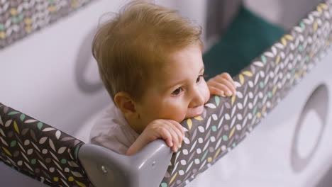 top view of caucasian baby in white bodysuit inside the baby playground while bitting the fabric of the park