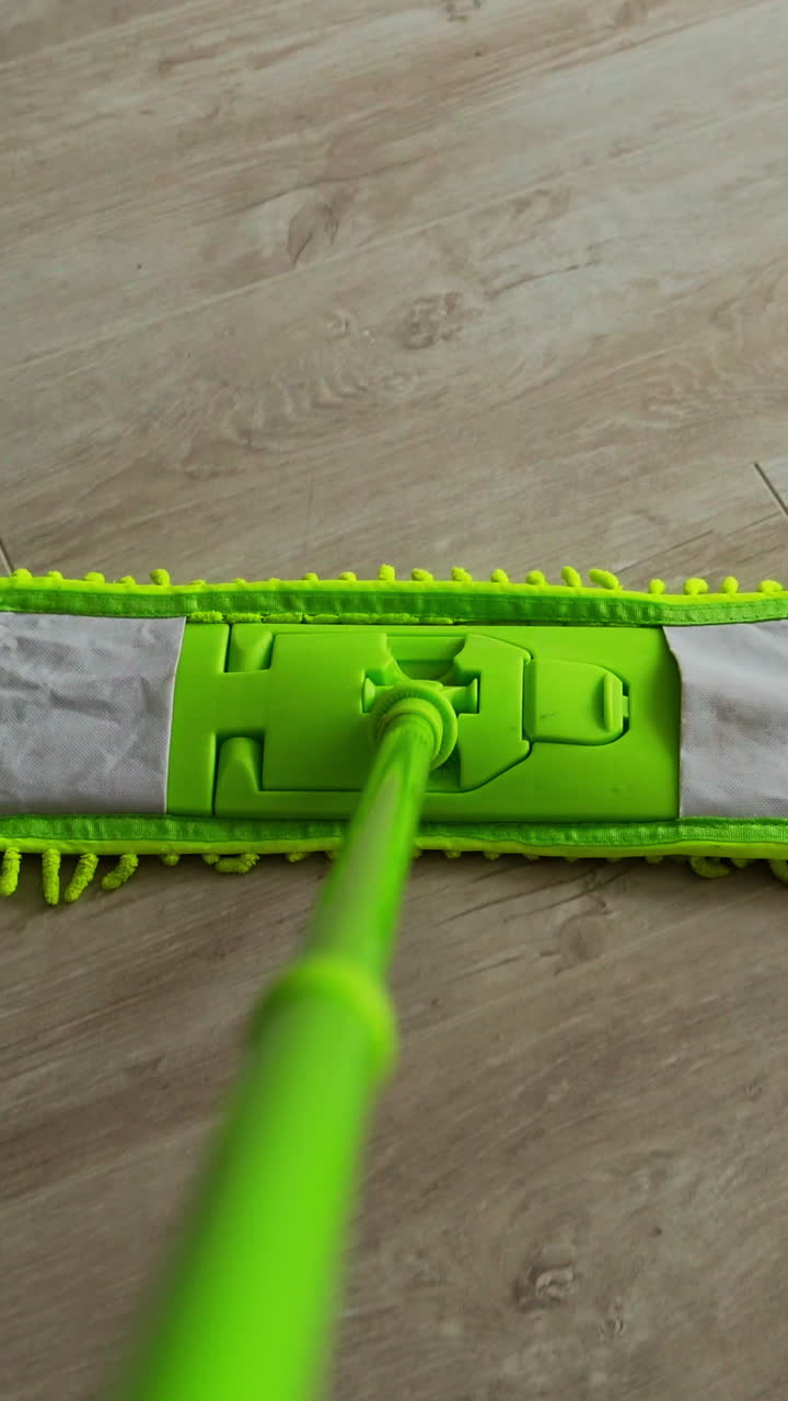 Cleaning the house. Green microfiber mop moving on the parquet floor to keep the house clean. Housekeeping concept. Close-up. Vertical video