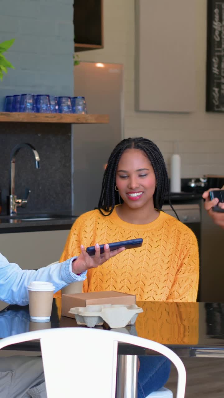 Vertical video: Laughing lady in yellow knit at cafe table, friends passing phones sharing posts