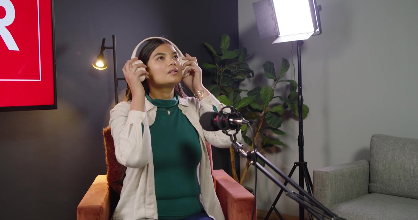 Donna afroamericana che entra, si sistema il top, si siede sul set, regola il microfono e indossa le cuffie per un podcast.