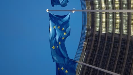 Vertical-video-of-European-flags-waving-at-night-in-front-of-the-Berlaymont-building,-the-headquarter-of-the-European-Commission-in-Brussels,-Belgium