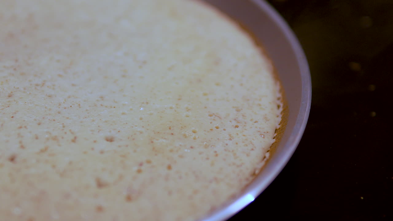 Macro di una crêpe sottile che cuoce in una padella, con bolle che si formano sulla superficie. Perfetta per tutorial di cucina e idee per la colazione