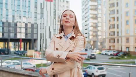 happy mature businesswoman using smartphone and looking at camera while standing on downtown street