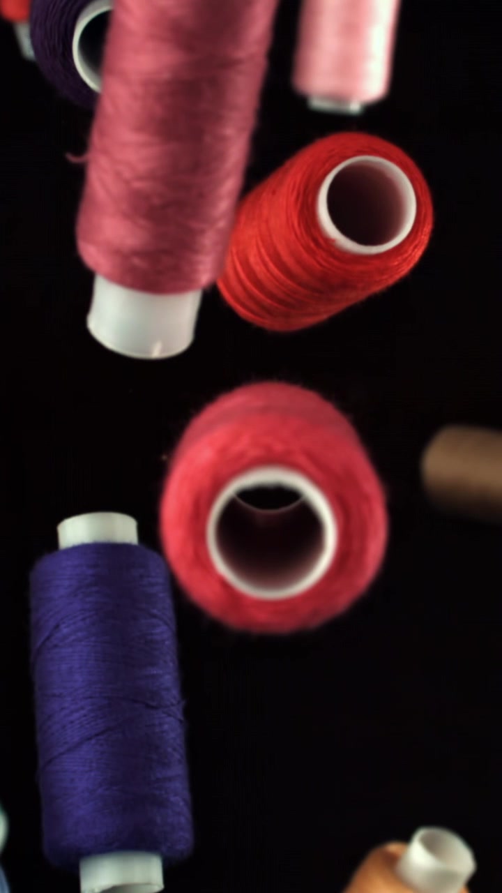 Colorful Spools of Thread Falling and Focusing on a Black Background