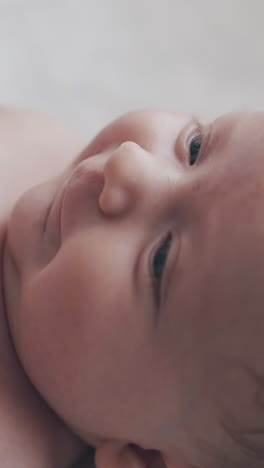adorable newborn boy with short fair hair and blue eyes lies in baby bed moves body and smiles extreme close view