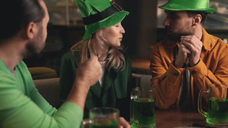 jeunes hommes et belle femme en chapeaux irlandais s'amusant avec des chopes à bière vertes