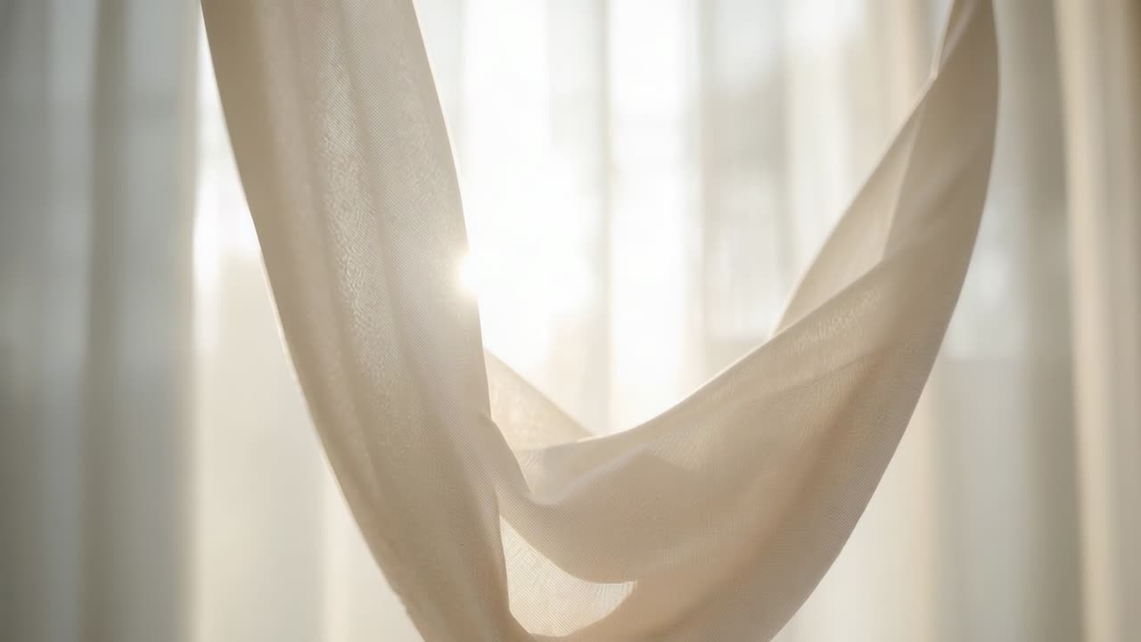 Sheer beige fabric panel shifting and lifting lower fold at backlit window as sunlight intensifies