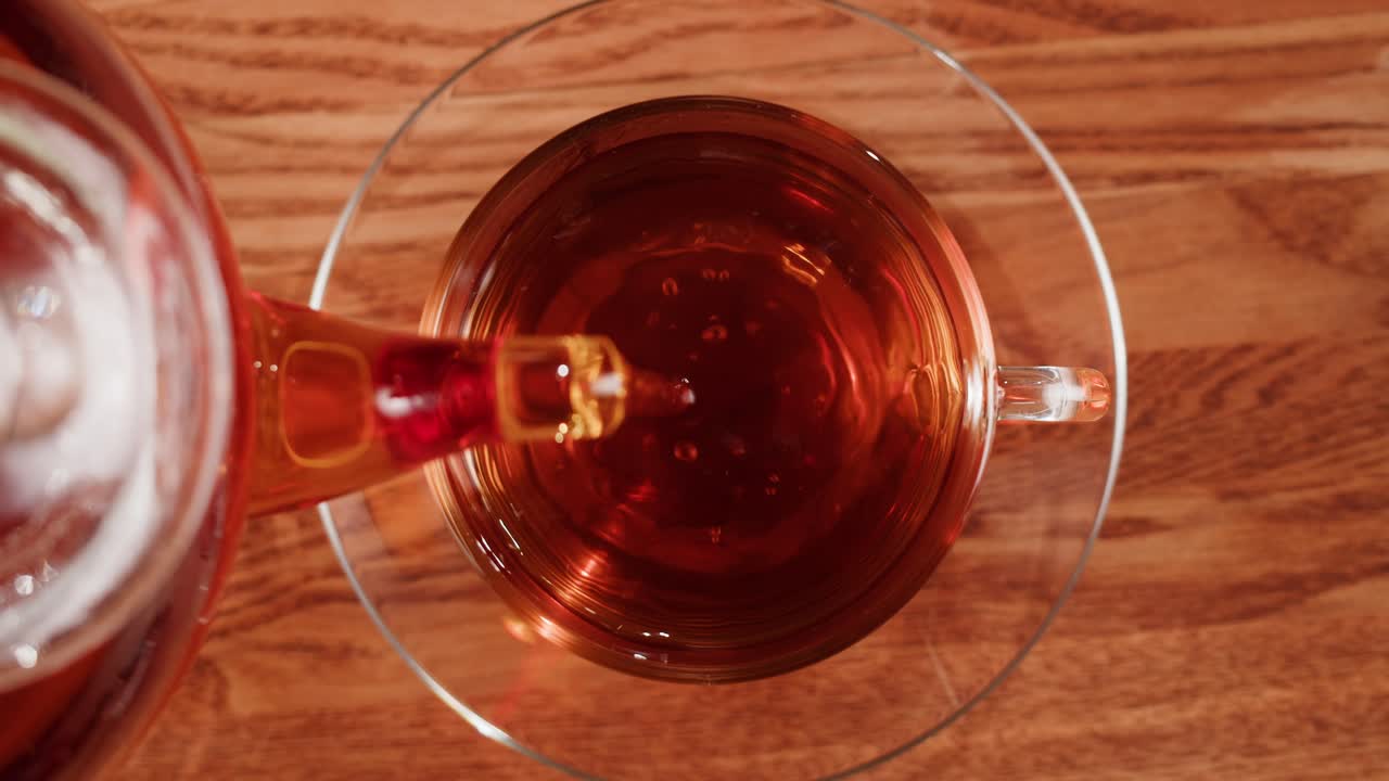 Pouring hot tea into a glass cup on a wooden table