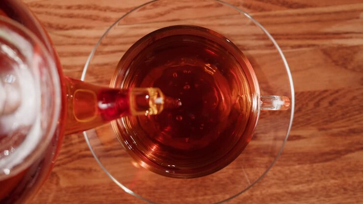 Pouring hot tea into a glass cup on a wooden table